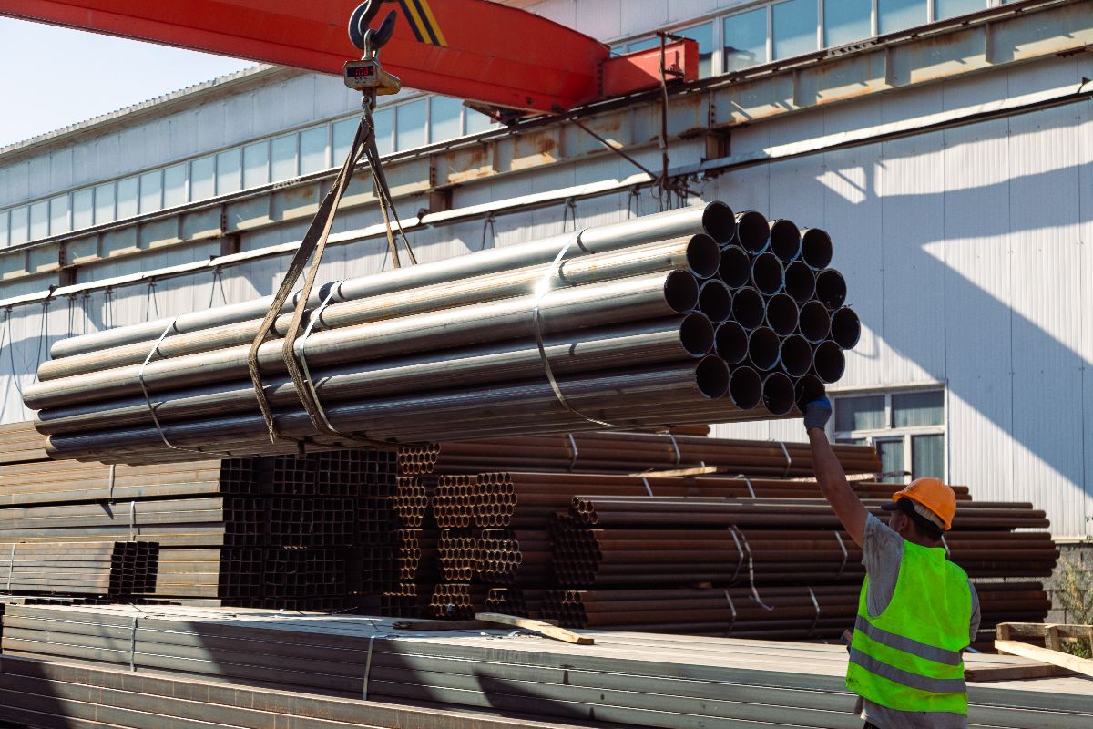 Worker guiding bundled black iron pipes during warehouse loading