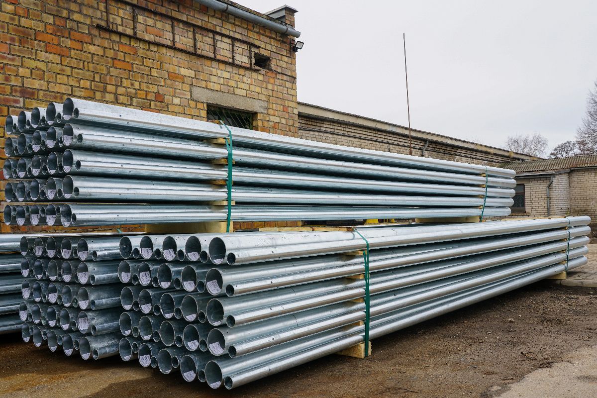 Galvanized pipes stacked outdoors beside a brick building for construction and industrial use