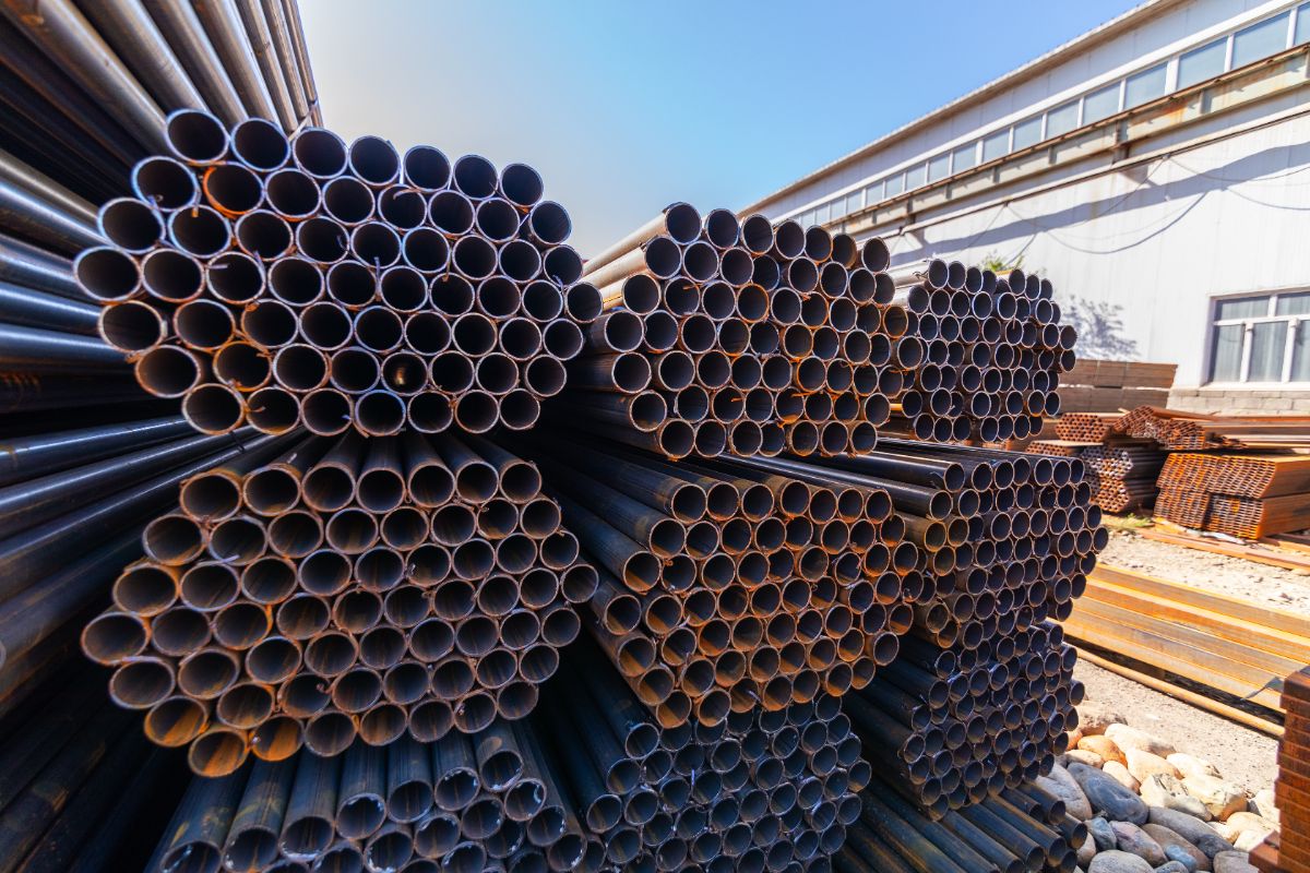Bundled GI pipes stacked outdoors near an industrial building for urban construction projects